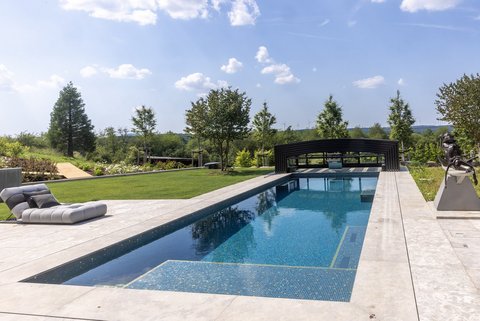 Die Sonne scheint auf einen klaren, blauen Pool, umgeben von Rasen.