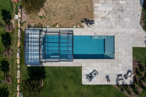 Vogelblick auf einen privaten Pool, dessen blau-goldene Mosaikfliesen in der Sonne glitzern.