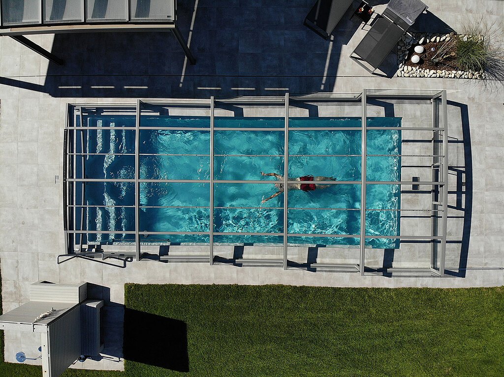 Drohnenshot auf einen modernen Pool mit der Poolüberdachung Limone Slim, im Pool schwimmt eine Person